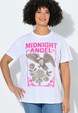 Mujer sonriente con pelo rizado lleva una camiseta blanca con la inscripción "MIDNIGHT ANGEL" y una ilustración de un pájaro y una rosa en rosa y gris.