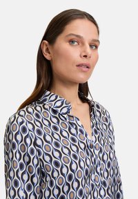 Blusa stampata con motivo ovale blu, nero e crema, colletto classico e patta con bottoni. Realizzata in tessuto leggero e morbido.