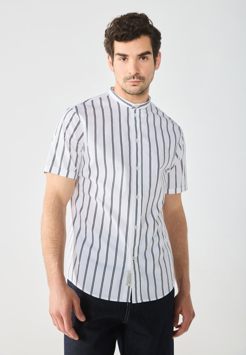 Short-sleeve, collared shirt in white with vertical black stripes, featuring a button closure and a slightly curved hem.