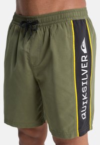 Shorts de bain verts avec panneaux latéraux noirs comportant un texte blanc "QUIKSILVER" et des accents jaunes. Taille à cordon et coupe décontractée.