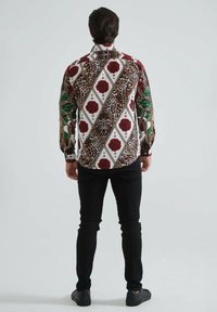 Chemise à manches longues arborant un motif audacieux de roses, d'imprimé léopard et de losanges géométriques en rouge, vert et blanc sur un fond clair.