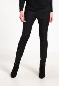 Svarta tapered byxor i slät tyg, med en stilren design, medelhög midja och sidofickor, matchade med svarta ankelboots.