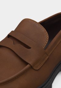 Mocassin en cuir marron avec bride pour monnaie et couture détaillée sur la tige, doté d'une semelle noire.