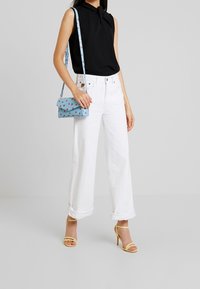 Haut noir sans manches, jean blanc à jambes larges, talons hauts jaunes à fines lanières, et sac bleu avec motif de cœurs rouges.