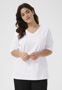 T-shirt blanc à col V avec manches courtes, présentant des accents texturés sur les manches et une coupe décontractée. Tissu doux avec une texture lisse.