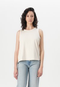 Top sin mangas color beige claro con escote redondeado, diseño sin mangas y tela suave, combinado con jeans azul claro.