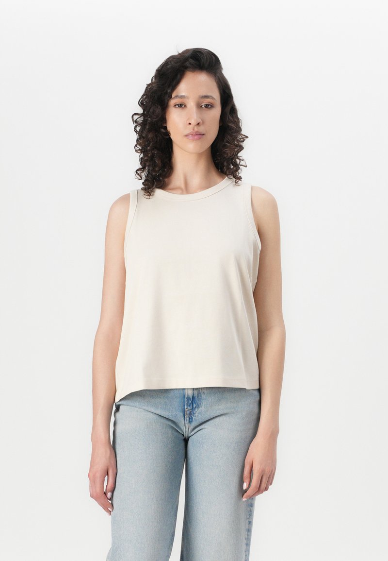 Top sin mangas color beige claro con escote redondeado, diseño sin mangas y tela suave, combinado con jeans azul claro.