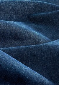 Tissu en denim bleu foncé à texture lisse, présentant des fils clairs subtils et une apparence légèrement froissée, mettant en avant les motifs de plis.