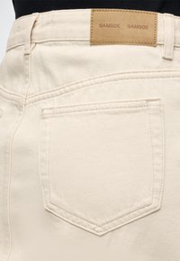 Πλάτη μπεζ τζιν παντελονιού που δείχνει μια μόνο πίσω τσέπη και ταμπόν από δέρμα ταμπά με την ένδειξη "SAMSOE SAMSOE" στη μέση.