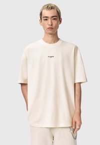 Krämfärgad oversize t-shirt i bomull med rund halsringning och korta ärmar. Texten "ALLSAINTS" i svart centrerad på bröstet.