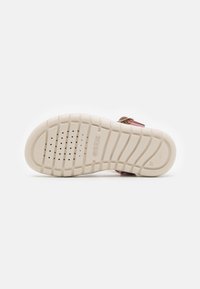 Chaussures avec une semelle extérieure en caoutchouc texturé, de couleur beige clair, dotées de perforations de ventilation et d'un logo en relief. Conçues pour le confort et la durabilité.