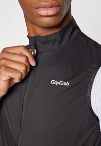 Zwarte fietsvest met hoge kraag, rits en GripGrab-logo; heeft een gestructureerde afwerking en ademend wit mesh-paneel aan de zijkant.