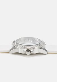 Orologio argento con quadrante rotondo testurizzato, cinturino in silicone bianco, dettagli in cristallo attorno alla ghiera e una corona sul lato.