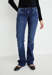 Dunkelblaue Jeans aus Denim mit weit auslaufendem Bein, vorderen Taschen und einem Knopfverschluss. Tragen Sie dazu schwarze Ballerinas mit silbernen Nieten.