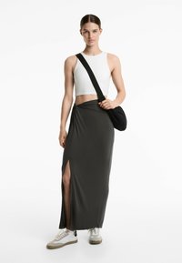 Gonna maxi in tessuto grigio scuro con uno spacco frontale, abbinata a un crop top bianco e sneaker grigie. Una borsa a tracolla nera aggiunge contrasto.