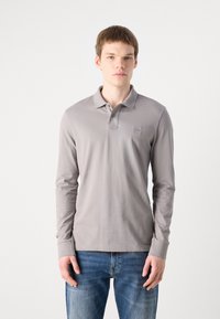 Long-sleeve gray polo shirt made of cotton, featuring a classic collar, button placket, and small logo detail on the chest. Denim jeans complement the look.