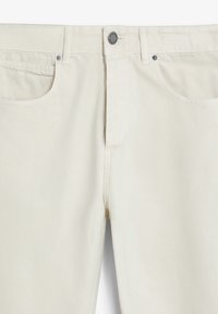 Jeans de mezclilla beige con cremallera, cierre de botón, cinco bolsillos y detalles de costura sutiles. Textura suave y corte ajustado.
