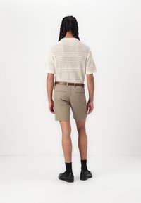Strikket polo-shirt i off-white med åbent vævdesign; brune shorts med bæltesløjfer; sorte sko og sokker; set fra ryggen.
