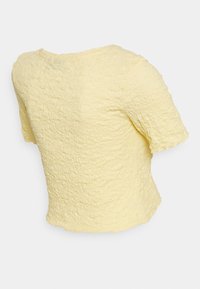 Gul kortärmad topp med texturerad tyg som har ett rynkigt mönster, rund nacke och en något lös passform vid fållen.
