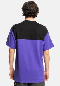 Tričko s krátkým rukávem s černou horní částí a fialovou dolní částí, vyrobené z texturované tkaniny s uvolněným střihem.
