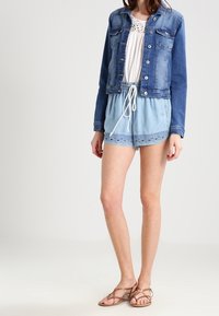 Denimjacka med knappstängning och två bröstfickor, kombinerad med en vit topp och ljusblå shorts med ögla och dragsko i midjan.