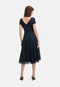 Robe bleu marine avec des manches courtes, dos en V, jupe évasée et finition pailletée texturée. Tissu lisse avec un ourlet en tulle superposé.