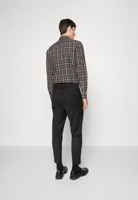 Zwarte, op maat gemaakte broek en een meerkleurig geruit overhemd met lange mouwen en een knoopsluiting, gezien vanaf de achterkant.