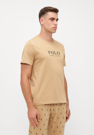 Homokszínű pamut póló klasszikus kerek nyakkivágással, az elején fekete nyomott "POLO RALPH LAUREN" logóval. Passzoló mintás nadrággal viselve.