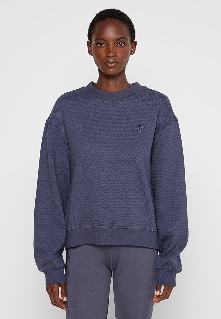 Donker marineblauw oversized sweatshirt met een gestructureerde wafelstructuur, ribbelkraag en -manchetten; heeft een klein logo op de borst.