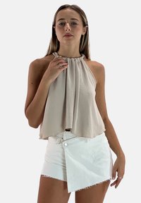 Top halter beige chiaro con scollo arricciato e design morbido, abbinato a shorts in denim bianchi asimmetrici con chiusura a un bottone.