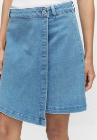 Vaaleansininen farkkuhame, jossa on etupainike sulkeminen, epäsymmetrinen helma ja hieman haalistunut tekstuuri. Klassinen viisi-taskumalli.