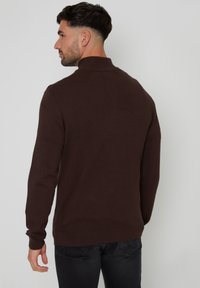 Maglione marrone lavorato a maglia con maniche lunghe e collo alto. Texture liscia, design aderente e dettagli a coste sui polsini e sull'orlo.