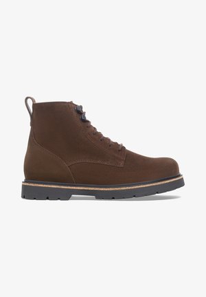 Bottine à lacets en suède marron avec semelle crantée en caoutchouc noir et languette à l'arrière, présentée de profil sur fond blanc.
