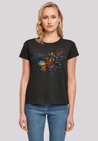 Black t-shirt featuring a colorful butterfly graphic with orange, blue, and yellow accents. Short sleeves and a round neck design.
