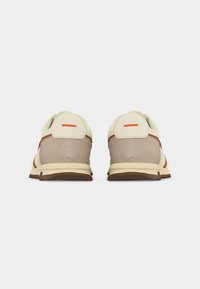 Paire de baskets beige et marron vues de dos sur un fond blanc avec des lignes horizontales orange près des languettes de talon.
