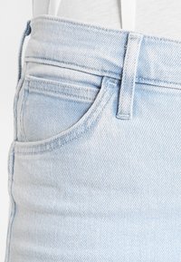 Jeans de denim azul claro con una textura suave, que cuentan con un bolsillo frontal, costuras visibles y un diseño sencillo.