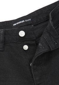 Černé džíny z denimu s hladkou texturou, vybavené stříbrnými knoflíky a štítkem s nápisem "THE KOOPLES JEANS." Čistý design, volný střih.