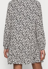 Zwart bloemenjurk met lange mouwen, voorzien van een patroon van kleine witte bloemen, een verzamelde rok en elastische manchetten. Zachte stoftextuur.