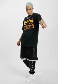 Sort T-shirt med grafisk design i orange og gult; sorte mesh shorts med hvide detaljer; hvide sneakers; sølv kædetrøje.