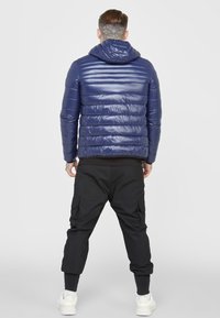 Mörkblå vadderad jacka med huva, med quiltad design och glansig yta. Kombinerad med svarta cargobyxor och vita sneakers.