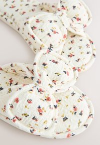 Chaussons blancs doux en tissu matelassé, petit motif floral rose et jaune, avec un grand nœud dessus.