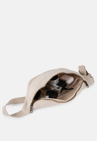 Beige canvas bag with a zipper, containing a camera, sunglasses, and earbuds. Features a flat shape and fabric loop for easy carrying.