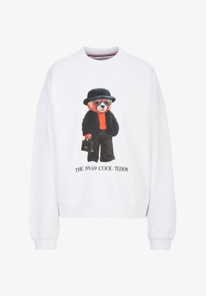 Witte trui met een teddybeer die een zonnebril, een zwarte hoed en jas draagt, een rood overhemd, en een kleine handtas vasthoudt met tekst eronder.