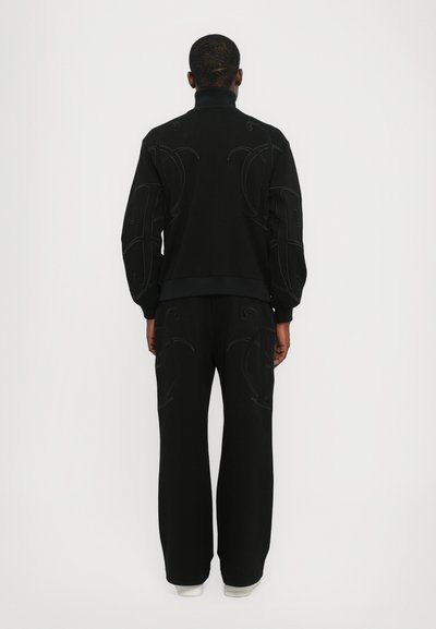 Ensemble de sweat-shirt et pantalon noir avec une broderie tonale complexe, présentant un col haut et une coupe ample avec des jambes larges. Tissu doux et texturé.