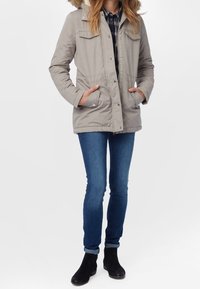 Světlé šedé péřové parkové s kapucí lemovanou kožešinou, čtyřmi předními kapsami a zapínáním na patentky. Nosit s modrými džínami a černými kotníkovými botami.