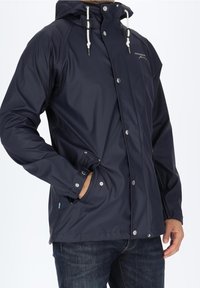 Veste imperméable marine avec capuche, fermetures à pression et cordon de serrage. Comprend des poches latérales et des poignets élastiques pour un ajustement sûr.