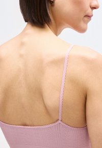 Κοντινό πλάνο του άνω μέρους της πλάτης και του ώμου μιας γυναίκας που φοράει ροζ υφασμάτινο τοπάκι με λεπτές τιράντες και κοντά καστανά μαλλιά.