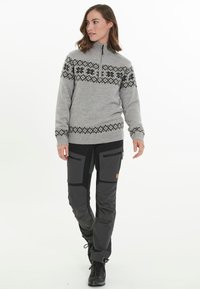 Grijze gebreide sweater met zwarte geometrische patronen, halve rits aan de voorkant en ribbels aan de mouwen, gecombineerd met donkergrijze nauwsluitende broek en zwarte laarzen.