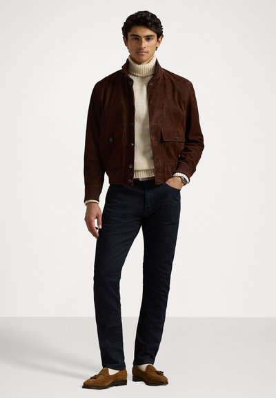 Rjava semiš jakna z dvema sprednjima žepoma, kremasto turtleneck pulover, temne kavbojke in rjavi semiš loafersi. Preprost dizajn, teksturiran material.
