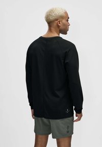 Czarna koszulka z długim rękawem z teksturowanym wzorem, rękawami raglanowymi i zaokrąglonym dołem. Połączona z szarymi szortami z nadrukowanymi napisami.